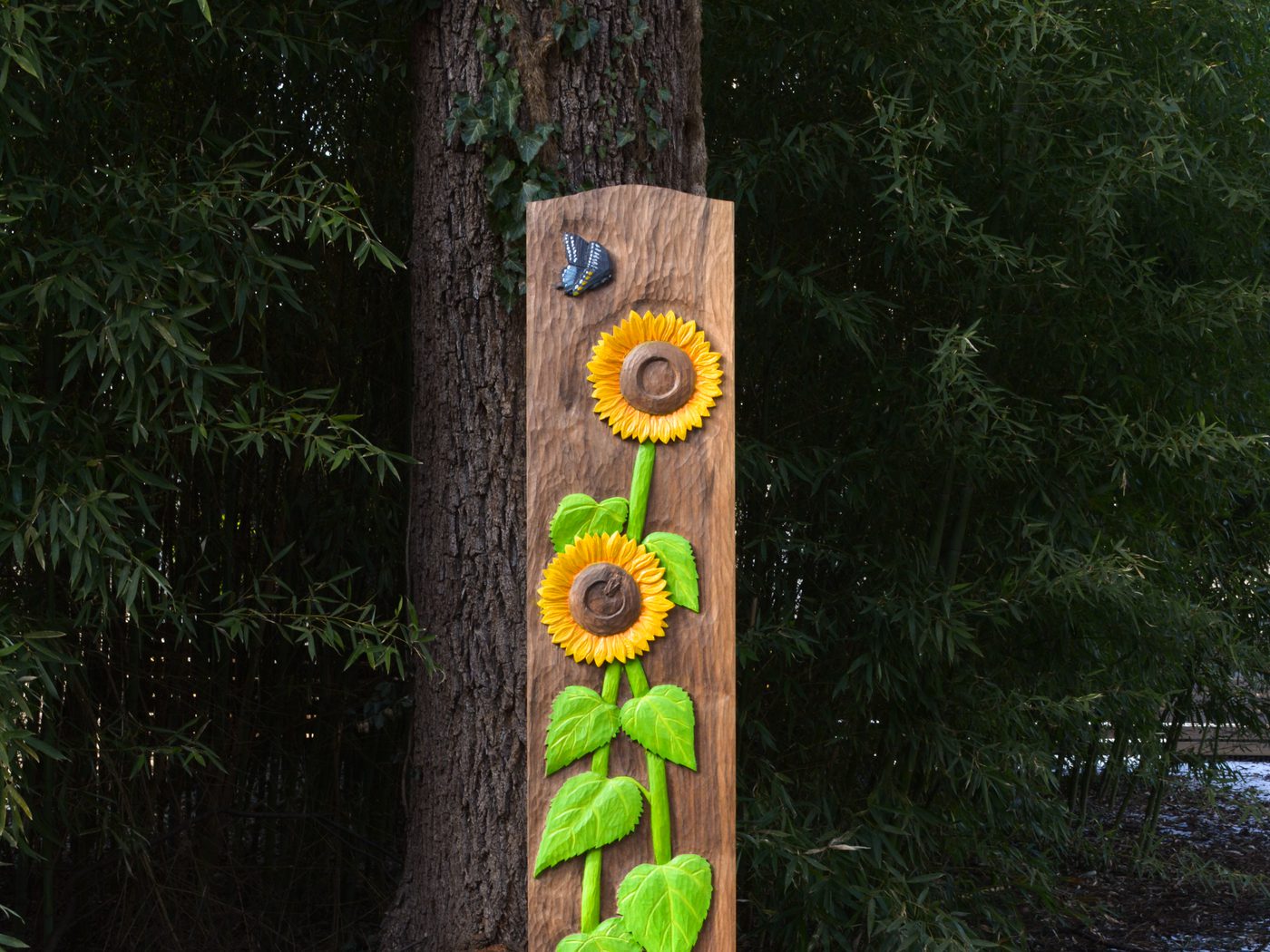 A bookcase side panel carved and painted by hand with sunflowers climbing a green stem