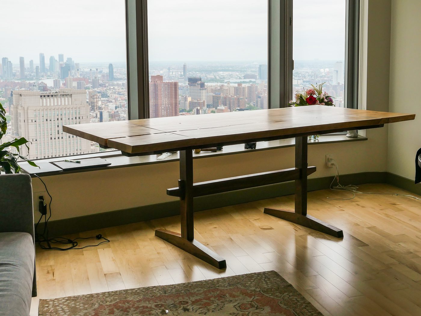 A symmetrical twin-pedestal trestle dining table in front of a wall of windows overlooking a city skyline