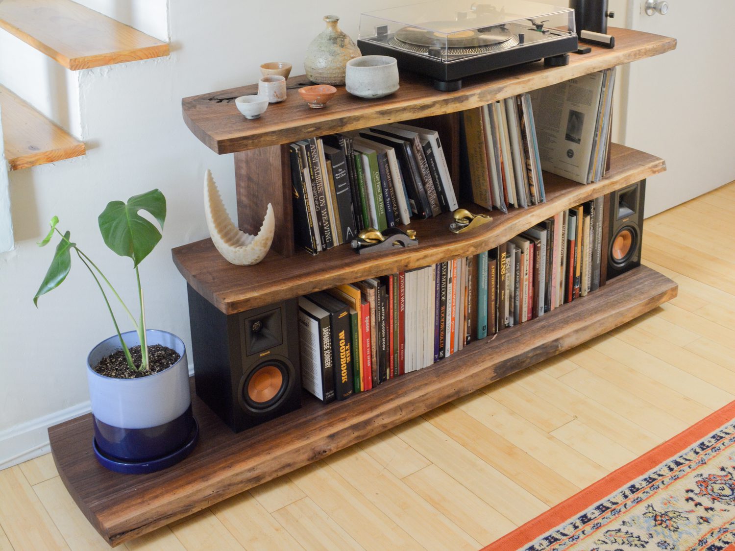 A live-edge walnut record console tucked under a staircase, a turntable on top and vinyl and books filed on the open shelves below