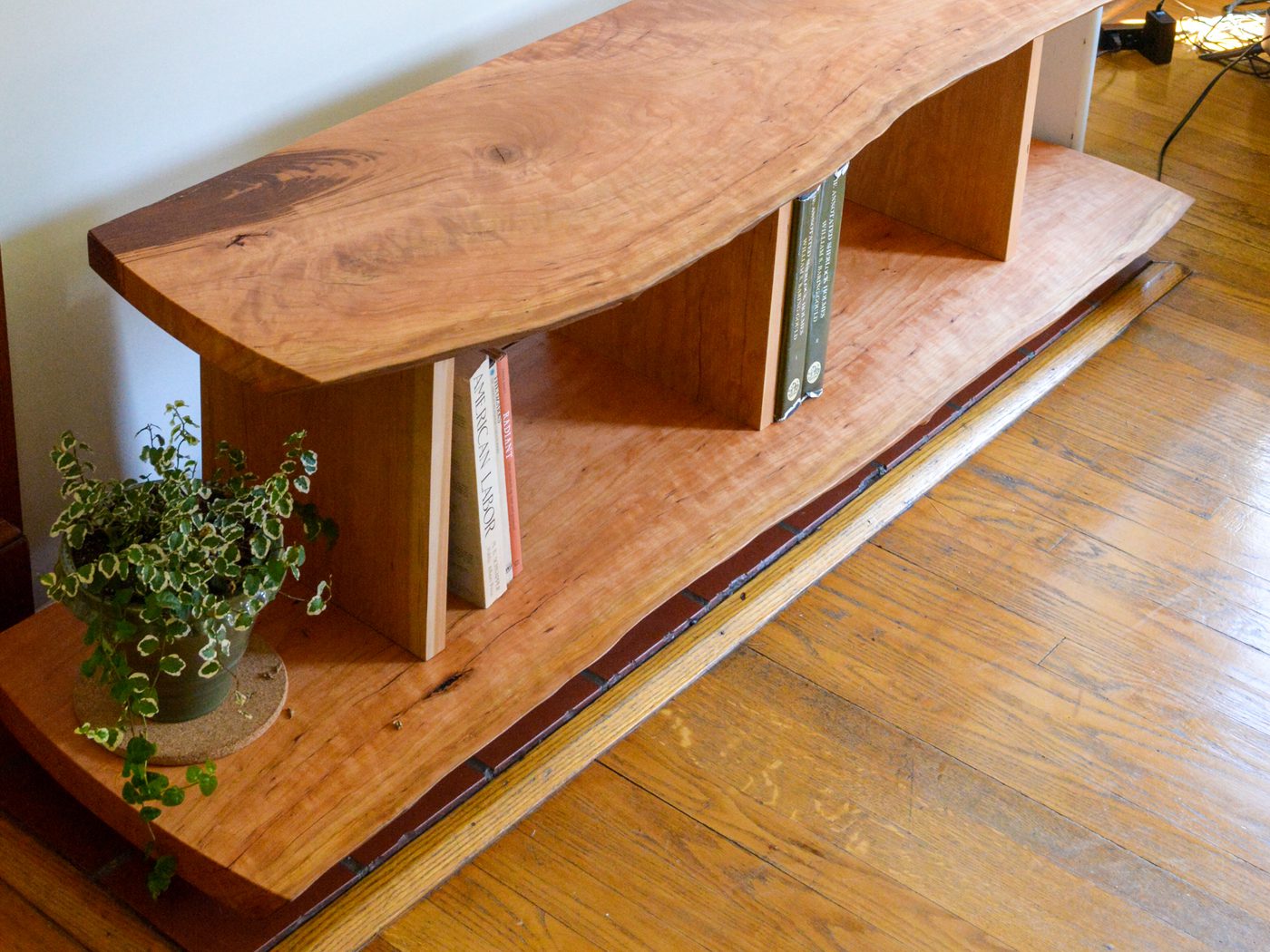 A long, low two-tier live-edge console with upright dividers splitting the lower tier into open compartments, set in front of a fireplace